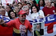 Pessoas em comício político. Homem com boné LULA segura foto de Lula, outro veste camiseta de Lula. Simone Tebet sorri.