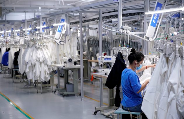 Trabalhadora em fábrica de vestuário com linha de produção e sistema transportador aéreo de roupas brancas.