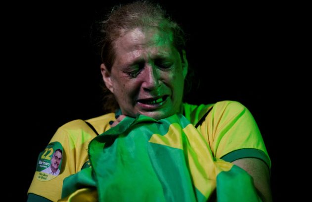 Mulher, apoiadora de Bolsonaro, chora com bandeira do Brasil. Usa adesivo do candidato.