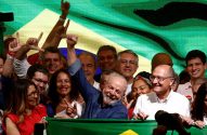 Lula sorri e ergue o punho em meio a apoiadores, com bandeiras do Brasil ao fundo e à frente.