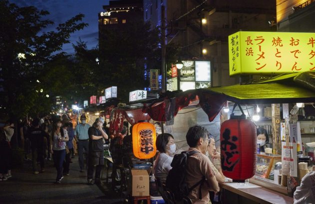 Noite no Japão: rua movimentada com barracas de comida (yatai) de Nakasu, iluminadas, e pessoas.
