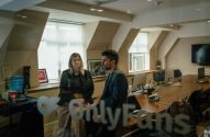 Mulher e homem conversam em sala de reunião da OnlyFans, com o logo da empresa visível no vidro.