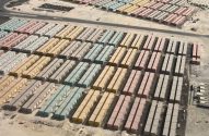 Vista aérea: centenas de módulos habitacionais coloridos em fileiras num vasto terreno arenoso com estradas.