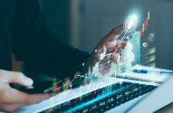 A imagem mostra as mãos de uma pessoa, que está sentada em frente a um notebook enquanto analisa ações ordinárias e preferenciais. Um gráfico de candlestick foi sobreposto digitalmente na imagem. (Foto: Shutterstock / Thapana_Studio)