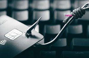 Cartão de crédito com chip fisgado por um anzol sobre um teclado.