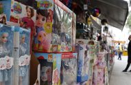 Caixas de brinquedos (bonecas e bichinhos) em exposição em uma banca de rua movimentada.