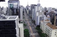 Vista aérea da Avenida Paulista em São Paulo, com edifícios altos e pessoas.