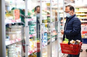 homem mais velho olhando vitrine de mercado enquanto segura cesta de compras