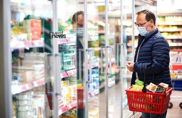 homem mais velho olhando vitrine de mercado enquanto segura cesta de compras