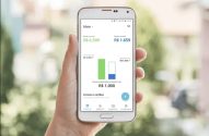 Mão segurando smartphone com app de finanças exibindo renda, gastos e economia mensal.