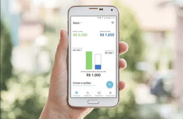Mão segurando smartphone com app de finanças exibindo renda, gastos e economia mensal.
