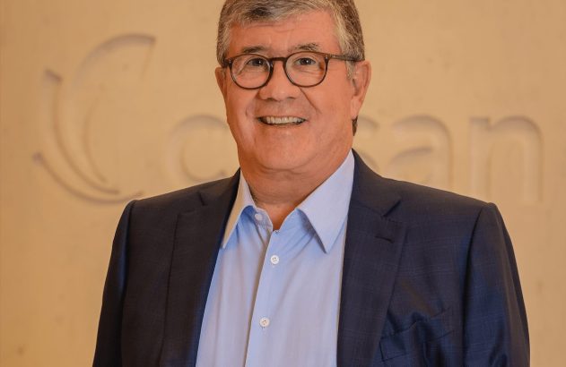 Retrato de homem sorrindo, de óculos e camisa azul, com logo da Cosan em relevo ao fundo.