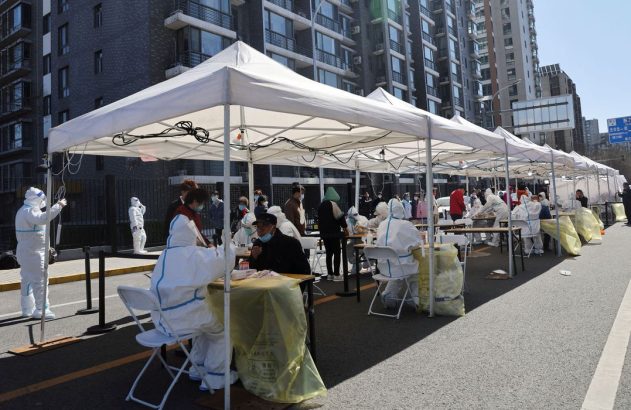 Pessoas em barracas brancas para teste de COVID-19 em rua de cidade.