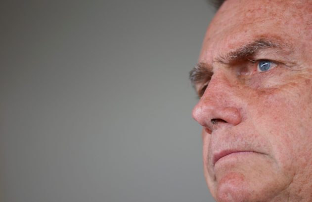 Close-up do perfil de um homem com olhos azuis, olhando à esquerda. Fundo cinza.