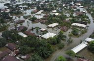 Vista aérea de um bairro residencial inundado, com casas e árvores parcialmente submersas na água marrom.