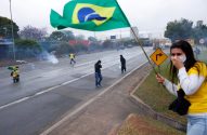 Protesto em rodovia: manifestante com bandeira do Brasil cobre o rosto em meio à fumaça. Pessoas reagem ao gás.