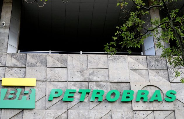 Letreiros verdes 'BR' e 'PETROBRAS' em fachada de concreto. Acima, entrada escura do prédio e árvore.