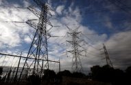 Torres de transmissão de energia de alta voltagem e cabos cruzando um céu azul com nuvens.