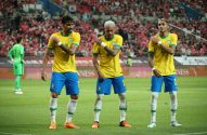 Três jogadores brasileiros de amarelo e azul comemoram em campo, mão no ombro.