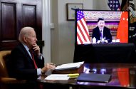 Joe Biden, pensativo, em videochamada com Xi Jinping, que sorri na tela com bandeiras EUA/China.