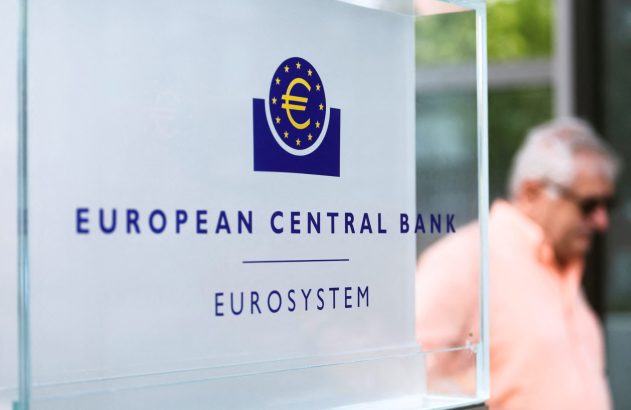 Placa do Banco Central Europeu com logo do euro. Pessoa borrada em segundo plano.