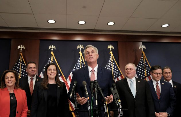 Kevin McCarthy fala em coletiva de imprensa com colegas e bandeiras dos EUA ao fundo.