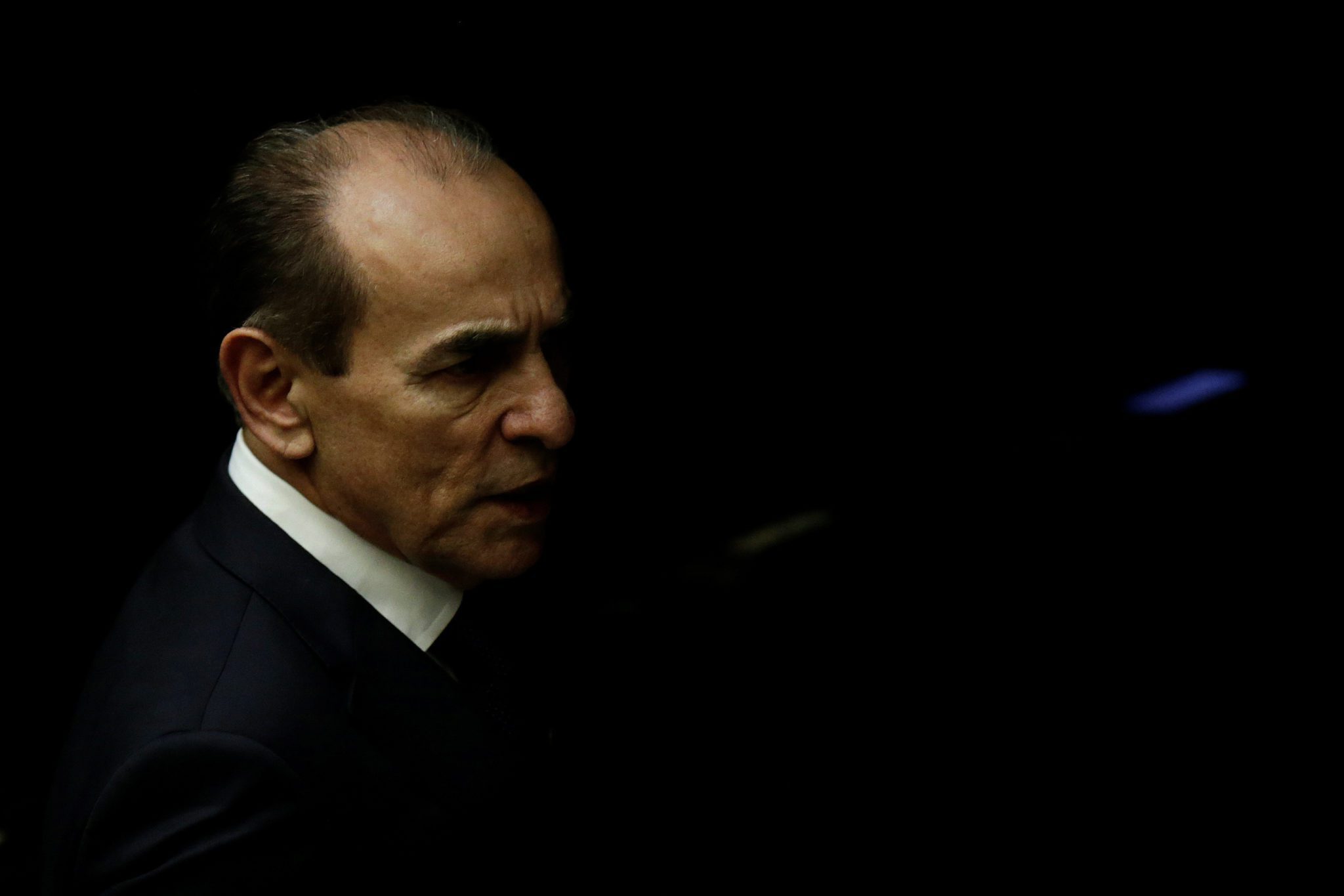 Homem de terno preto e camisa branca em um fundo escuro no Congresso Nacional