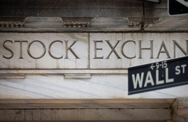 Letras "STOCK EXCHANGE" em prédio de pedra com placa da Wall Street em primeiro plano.