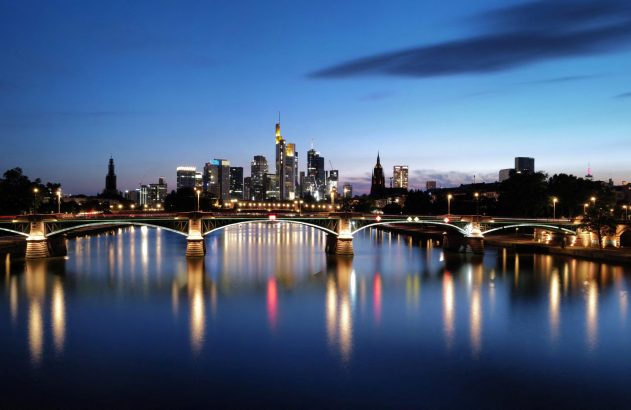 Frankfurt à noite: arranha-céus, ponte iluminada sobre o rio e reflexos brilhantes na água.