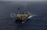Navio-plataforma de petróleo e gás flutuando em mar aberto, com outras embarcações ao longe.