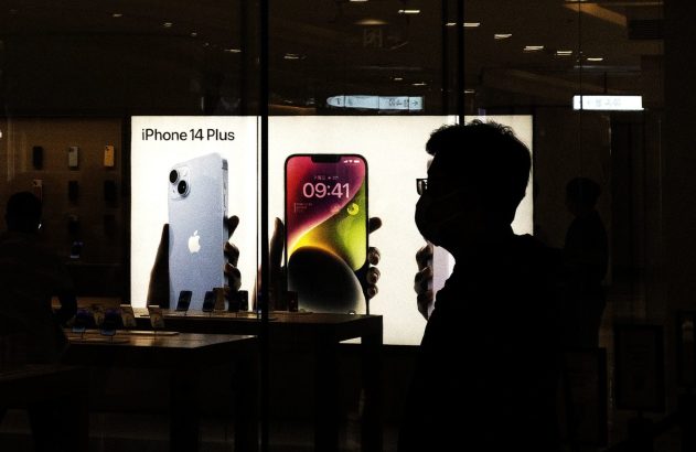 Pessoas em silhueta observam displays iluminados de iPhone 14 Plus em loja escura.