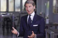 Homem de terno azul-marinho, cabelo grisalho, gesticula com as mãos abertas. Usa microfone de lapela e muitas pulseiras.