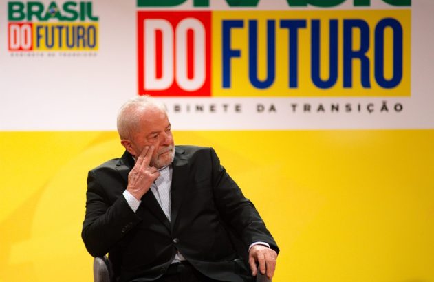 Lula, sentado, mão no rosto. Ao fundo, banners 'Brasil do Futuro' e 'Gabinete da Transição'.