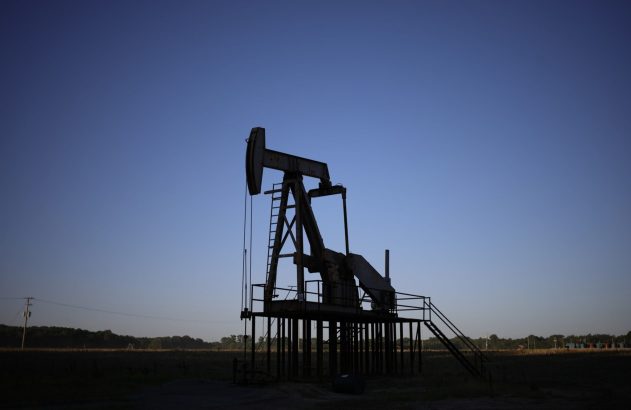 Silhueta de uma bomba de petróleo em campo aberto, sob um céu azul-escuro. A luz sugere amanhecer ou entardecer.