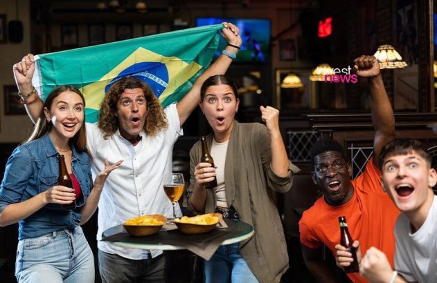 Torcedores brasileiros vibrando em um bar, com bandeira e bebidas.