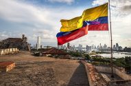 Bandeira da Colômbia tremulando sobre forte histórico e skyline de Cartagena à beira-mar.