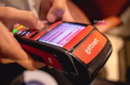 Mãos operam terminal de pagamento Getnet vermelho e preto, com tela e botões acesos.
