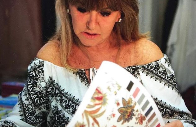 Mulher em blusa branca e preta examinando folha com estampas e amostras de cores.