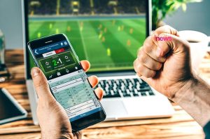 Pessoa usando celular com app de apostas de futebol, assistindo jogo em laptop; punho com 'news'.