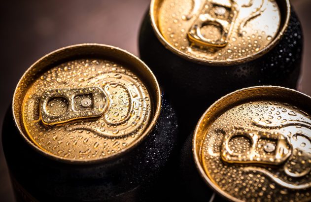 Três latas de bebida geladas com tampas douradas e gotas de condensação.