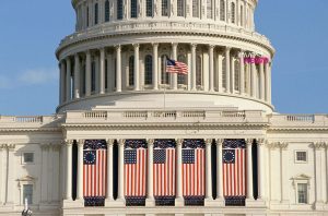 Cúpula e fachada do Capitólio dos EUA decoradas com bandeiras americanas, incluindo designs históricos.