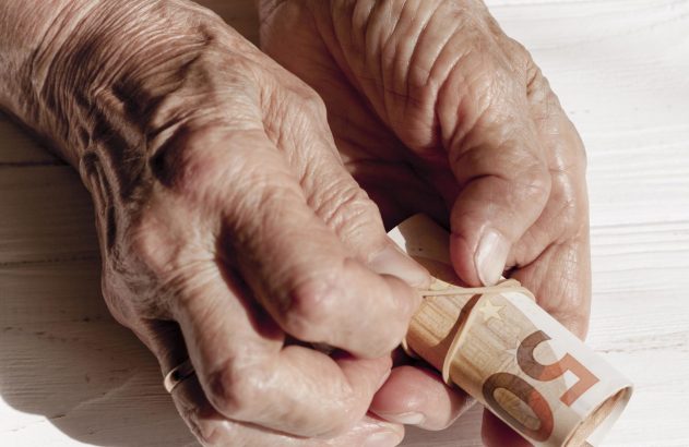 Mãos envelhecidas seguram um maço de notas de 50 Euros, presas por um elástico.