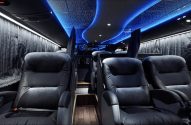 Interior espaçoso de ônibus executivo com assentos reclináveis de couro preto e iluminação ambiente azul no teto.