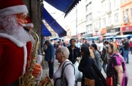 Estátua de Papai Noel com saxofone em rua comercial movimentada com pessoas.