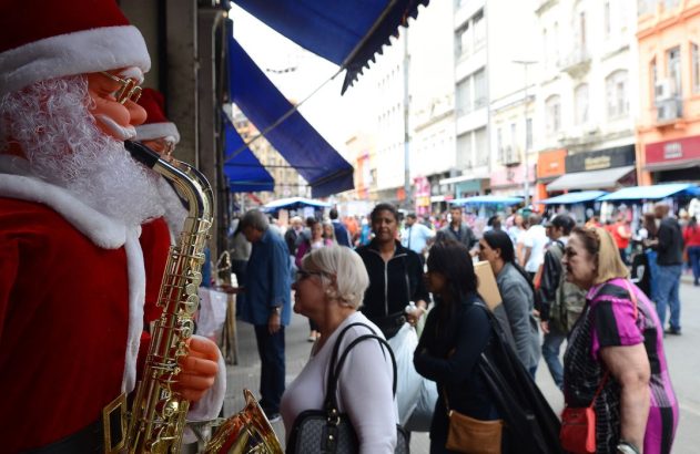 Estátua de Papai Noel com saxofone em rua comercial movimentada com pessoas.