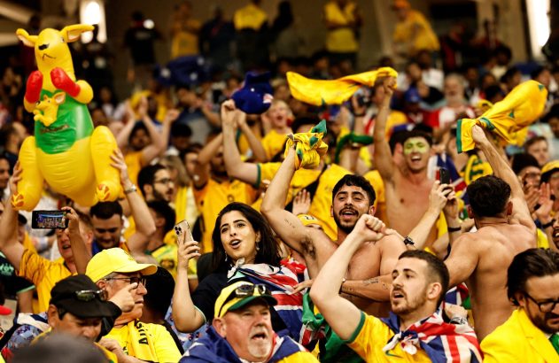 Torcida australiana animada com um canguru inflável e bandeiras erguidas em um evento.