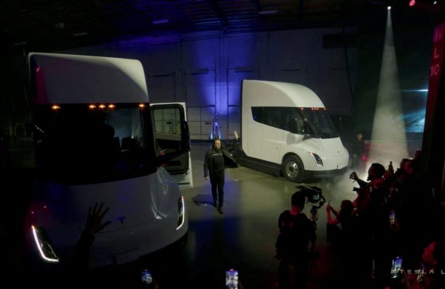 Evento de lançamento: Elon Musk entre dois Tesla Semi brancos. Público assiste.