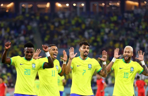 Quatro jogadores do Brasil de amarelo celebram, sorrindo e com mãos levantadas, em estádio com torcida.
