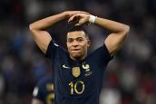 Kylian Mbappé, jogador da França, camisa 10, com as mãos acima da cabeça e expressão séria em jogo de futebol.