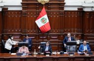 Membros do parlamento peruano em reunião. Um homem aponta enquanto outros usam dispositivos eletrônicos. Bandeira do Peru ao fundo.